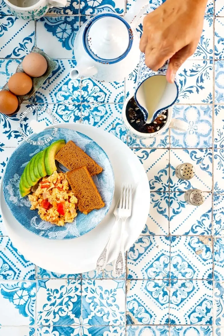 eggs, avocado and toast on a blue plate on a blue and white tiles table next to a teapot and tea cup