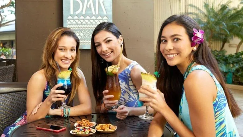 three women sitting at a table with tropical drinks in their hands