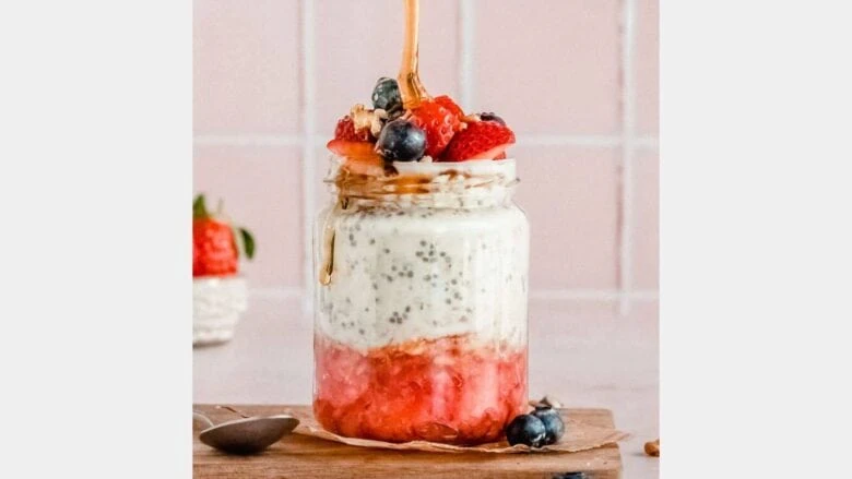 jar filled with pink berry compote layered with white overnight oats and topped with berries