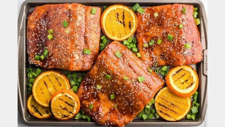 overhead shot of 3 filets of salmon next to grilled orange slices