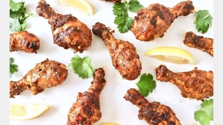 overhead shot of tandoori chicken drumsticks next to cilantro and lemon slices