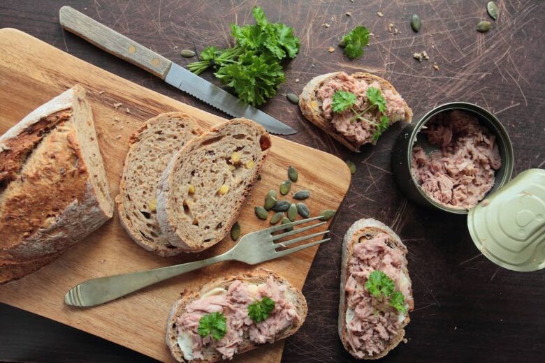 Overhead shot of wooden cutting board with bread on it next to a can of tuna