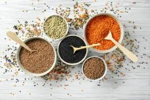 Shot from above of various sized bowl of different colored lentils with wooden spoons in the bowls