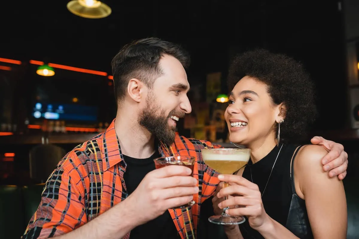 woman holding a pisco sour drink with a man holding a drink in a bar