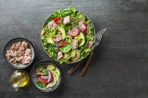 Overhead shot of green salad with tuna chunks on it next to canned tuna