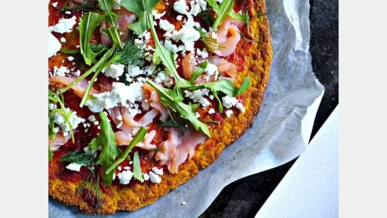 close up of pumpkin pizza topped with sauce, cheese and arugula 