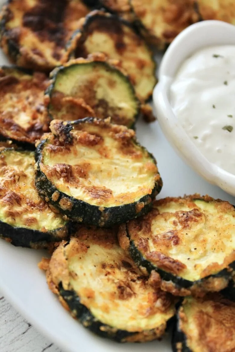 Air-fried zucchini chips with dip served on a plate.