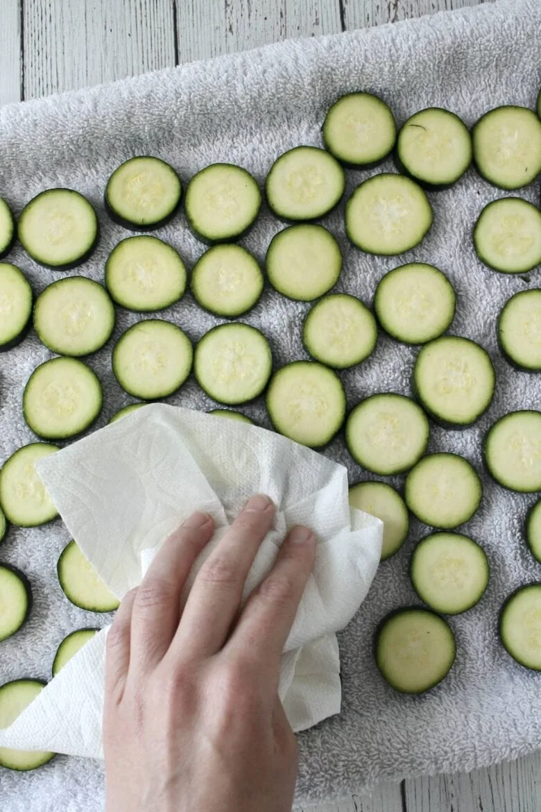 A person drying sliced zucchini on a towel.