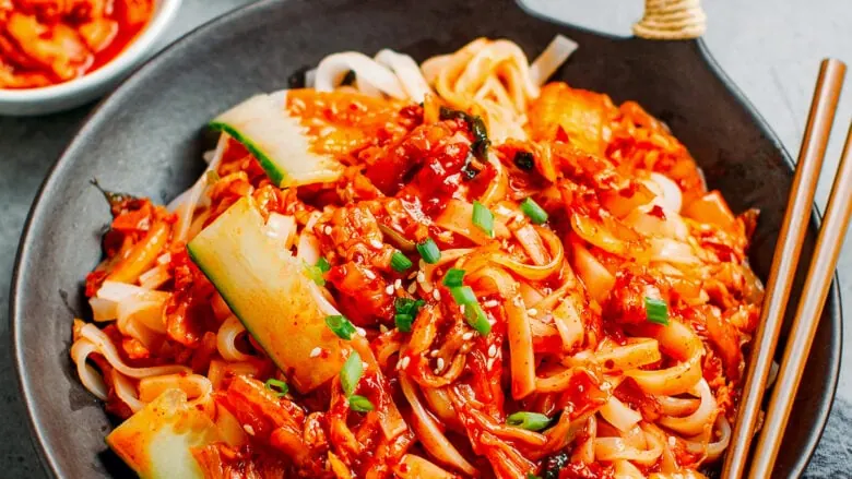A bowl of noodles with vegetables and kimchi.