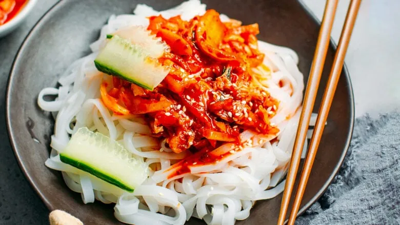 A plate with noodles and cucumbers garnished with kimchi.