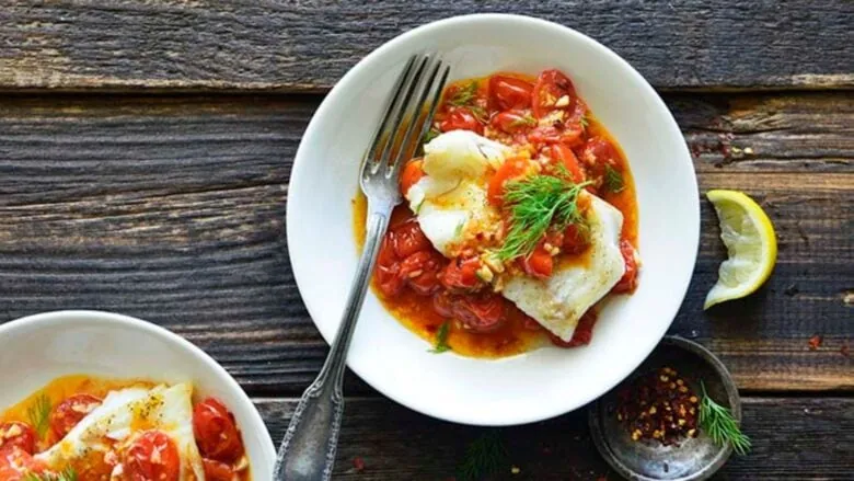 Two plates with fish and tomatoes on a wooden table.