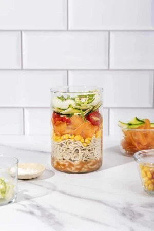 A glass jar filled with vegetables and noodles.