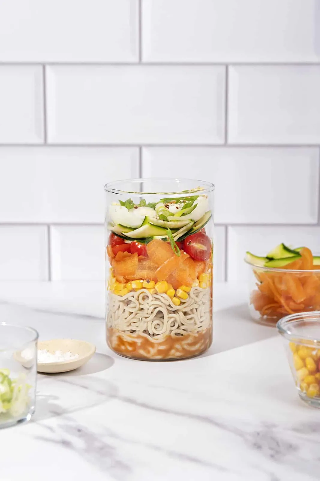 A glass jar filled with vegetables and noodles.