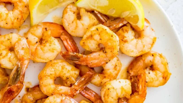 Grilled shrimp on a white plate with lemon wedges.