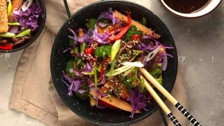 A bowl of red cabbage and broccoli with chopsticks.