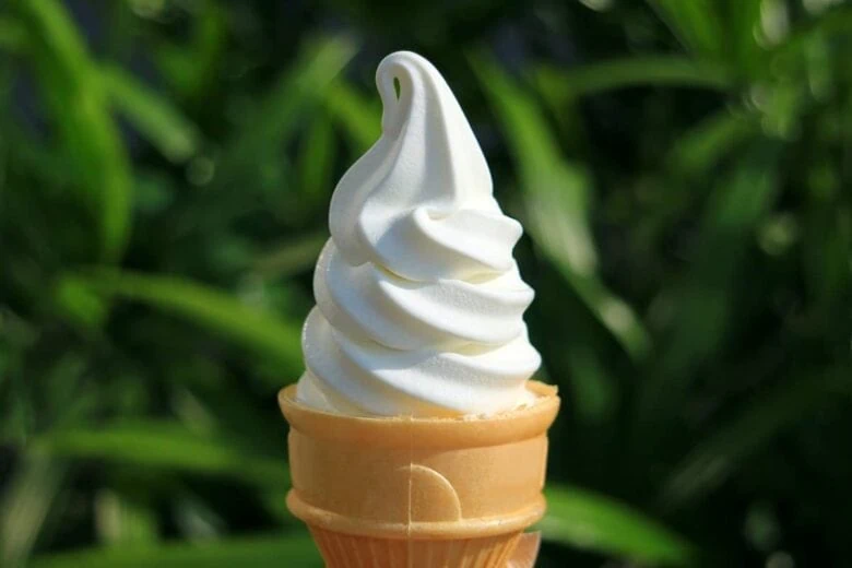 A person holding a cone of soft serve ice cream.