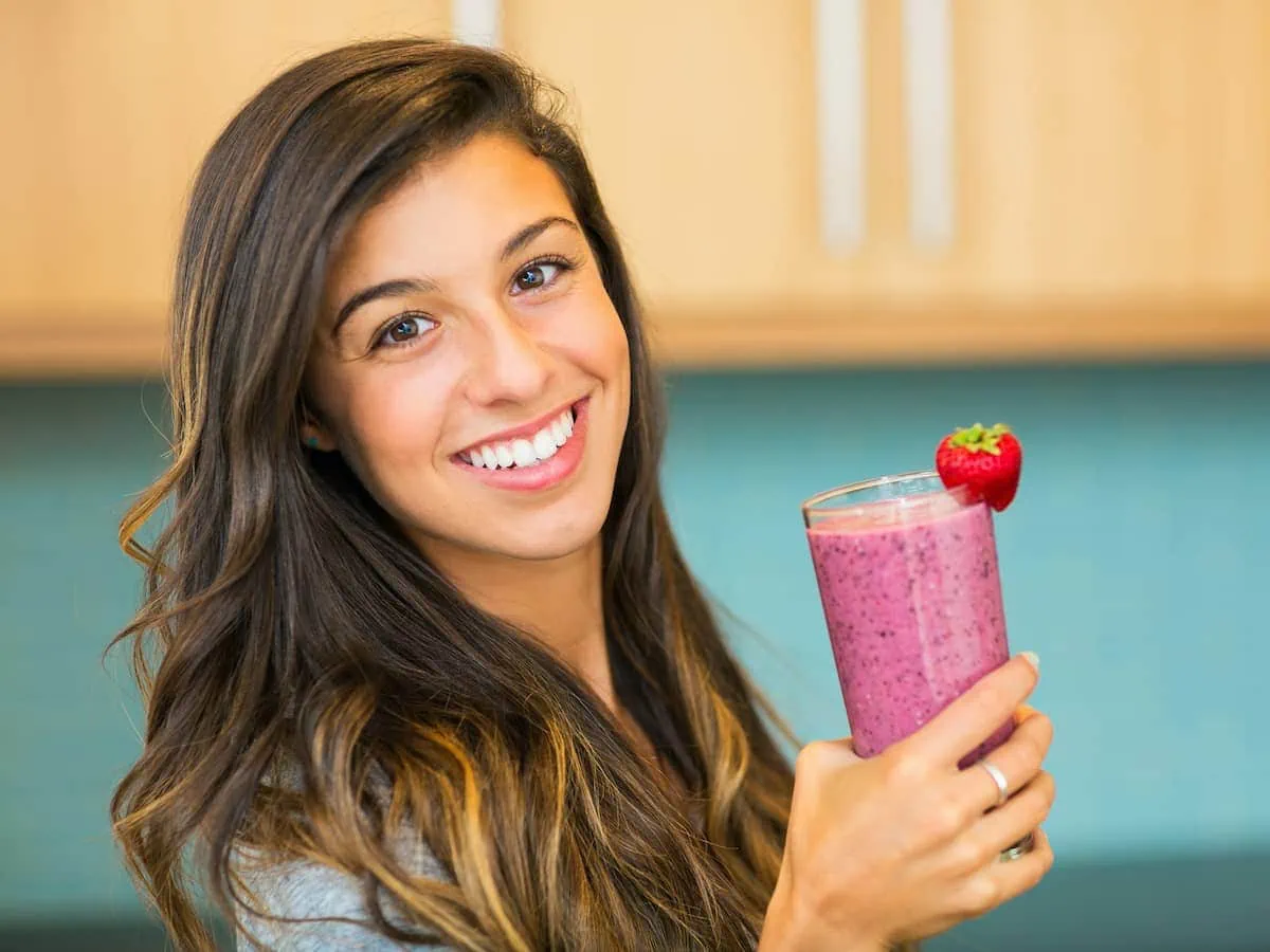 A woman holding an unhealthy smoothie with a strawberry in it.