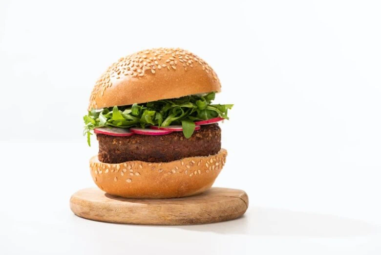 Veggie burger with lettuce and radishes on top of a wooden board.