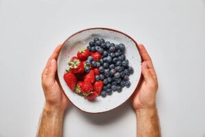 A man's hands holding a bowl of blueberries and strawberries.