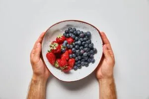 A man's hands holding a bowl of blueberries and strawberries.