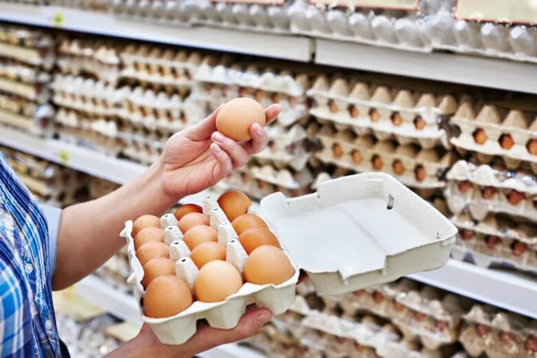 A woman is holding a carton of eggs at a store, contemplating what to buy at Costco.