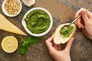 A person is putting pesto on a slice of bread.