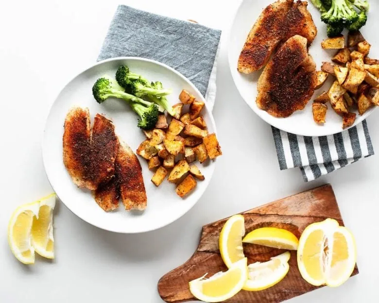 Two plates of fish with potatoes and lemons on a cutting board.