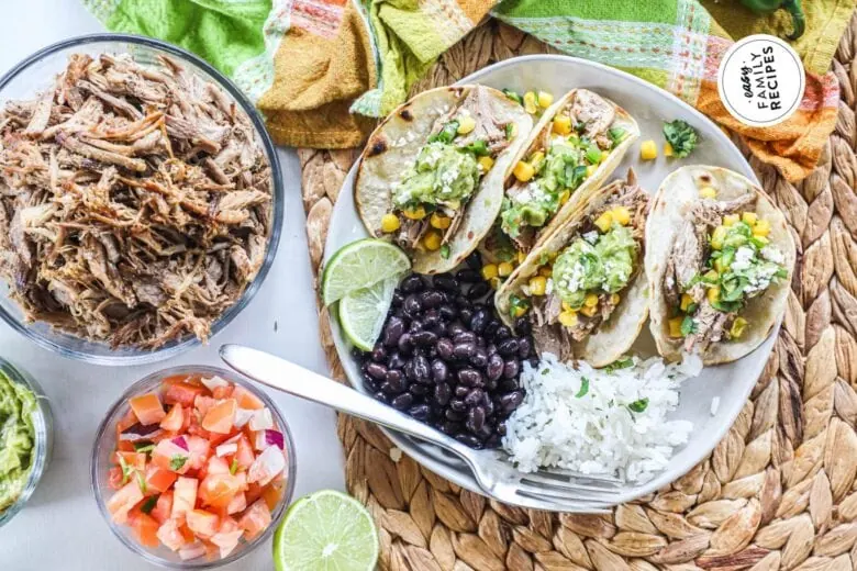 Pulled pork tacos on a plate with rice and beans.