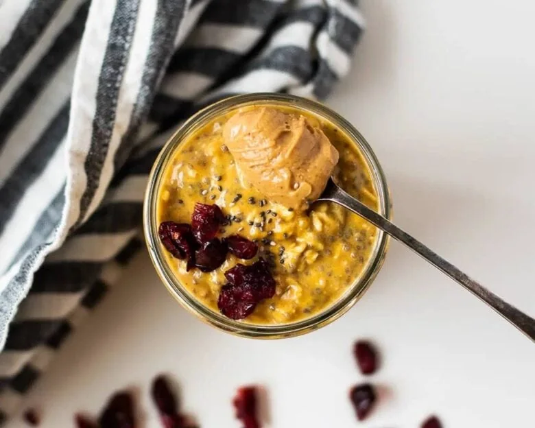 A jar of oatmeal with cranberries and peanut butter.