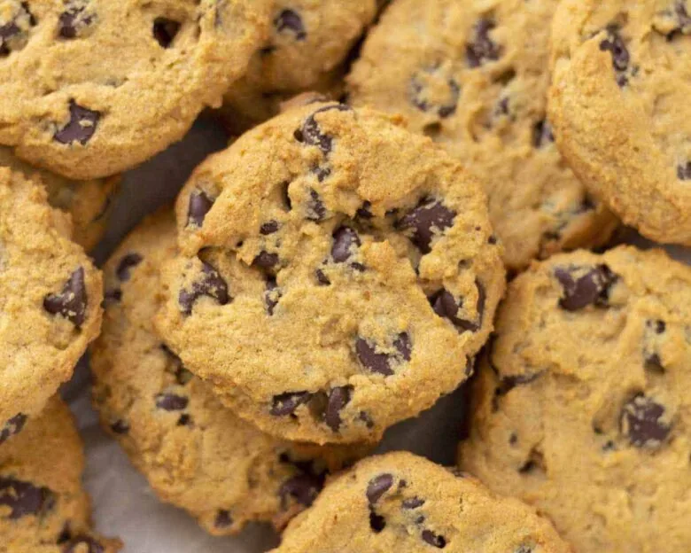 A pile of chocolate chip cookies on a piece of parchment paper.