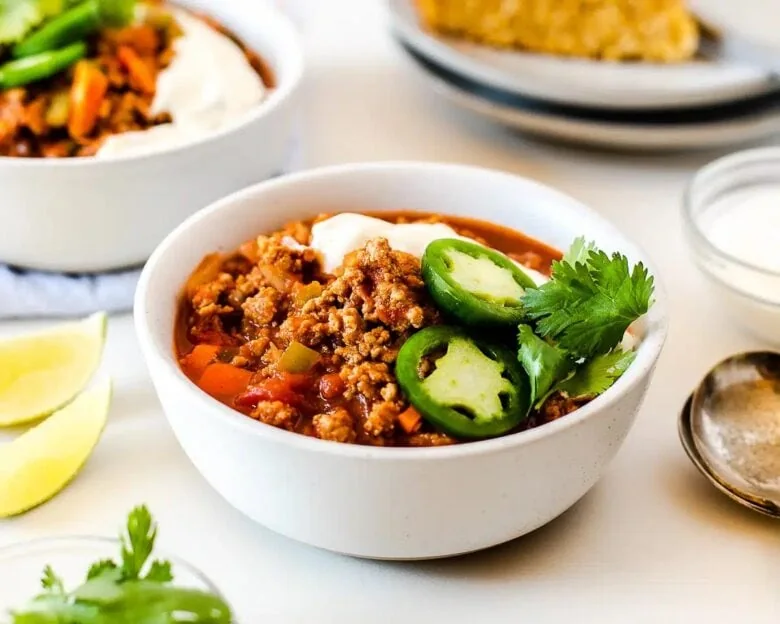 Two bowls of chili with sour cream and limes.