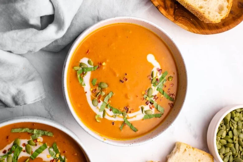 A bowl of pumpkin soup with sour cream and bread.