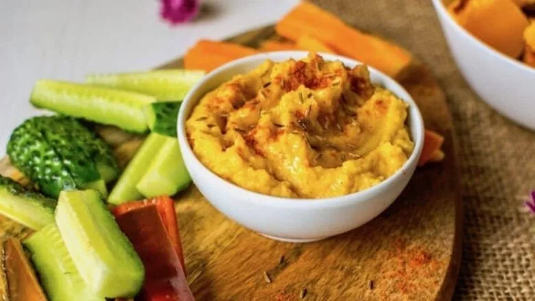 A bowl of hummus with carrots and cucumbers.