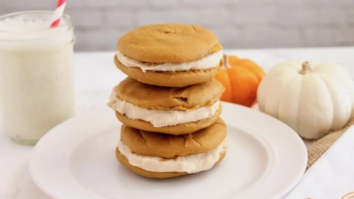 A stack of pumpkin ice cream sandwiches on a plate next to a glass of milk.