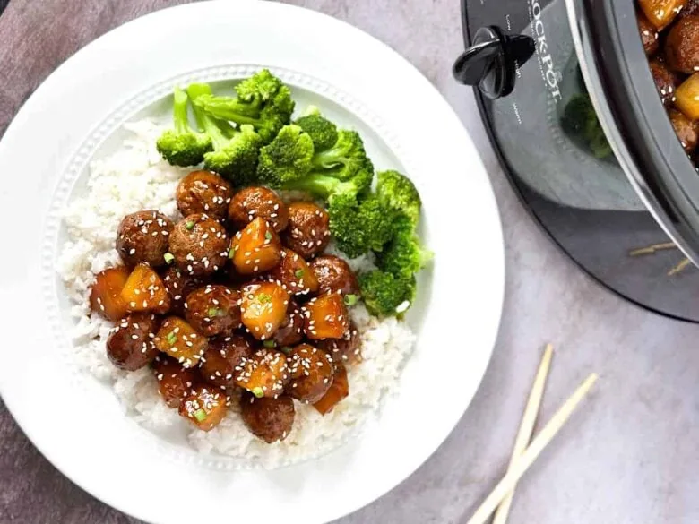 A plate with broccoli and meat on it next to a crock pot.