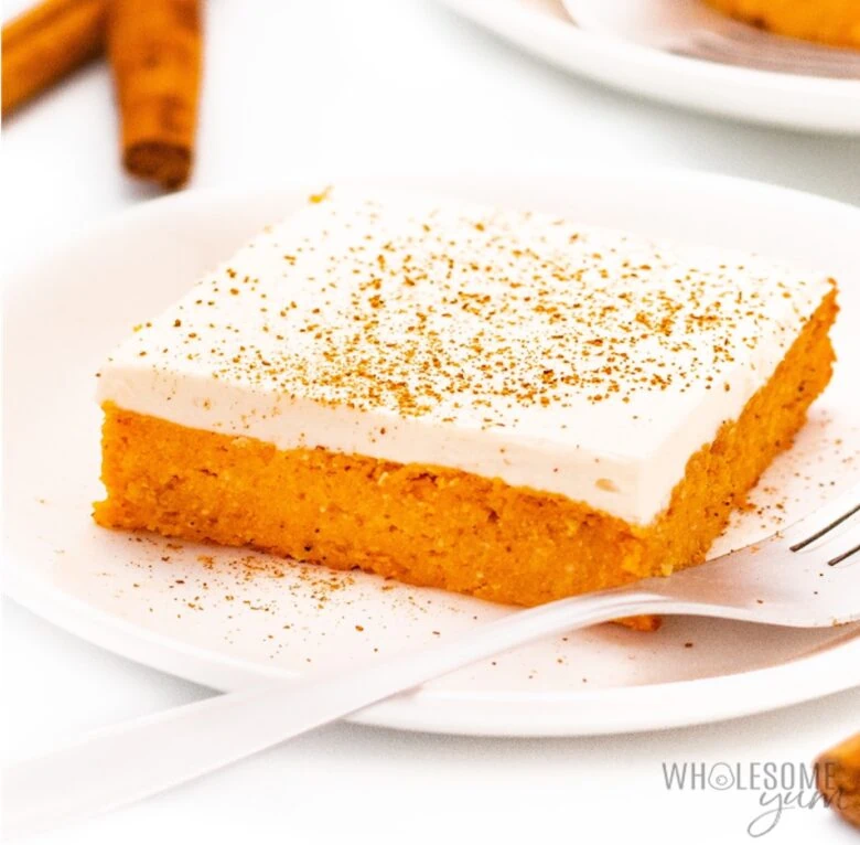 A slice of pumpkin cake on a plate with cinnamon sticks.