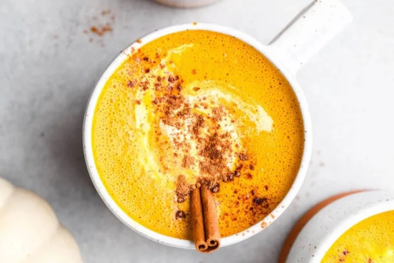 Pumpkin soup in a white bowl with cinnamon sticks.