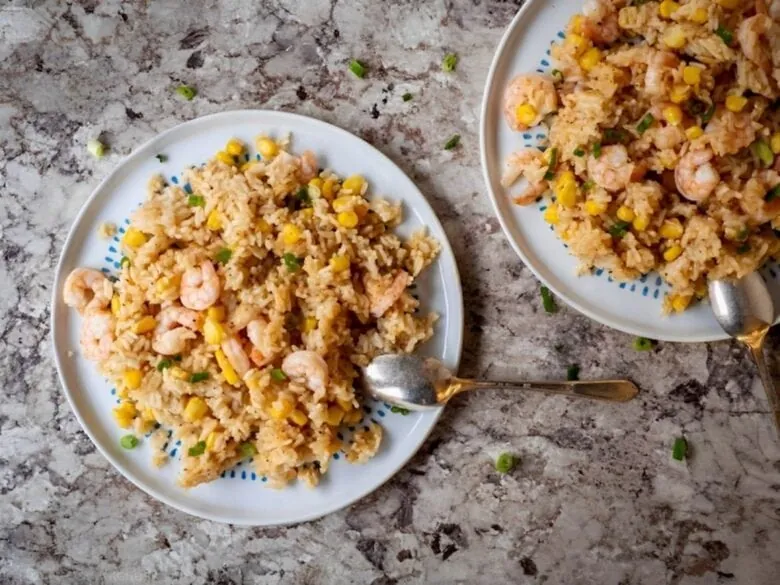 Two plates of fried rice with shrimp and corn.