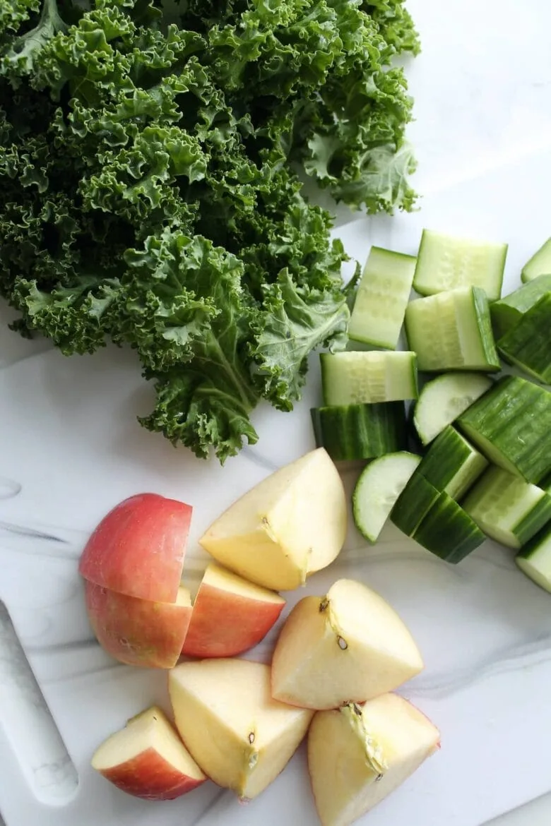 Kale, apples and cucumbers on a cutting board.