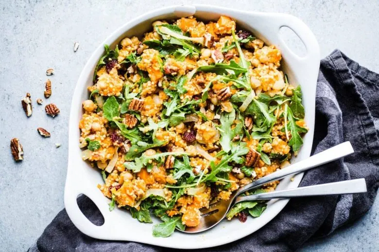 A white bowl filled with a salad with pecans, carrots and arugula.