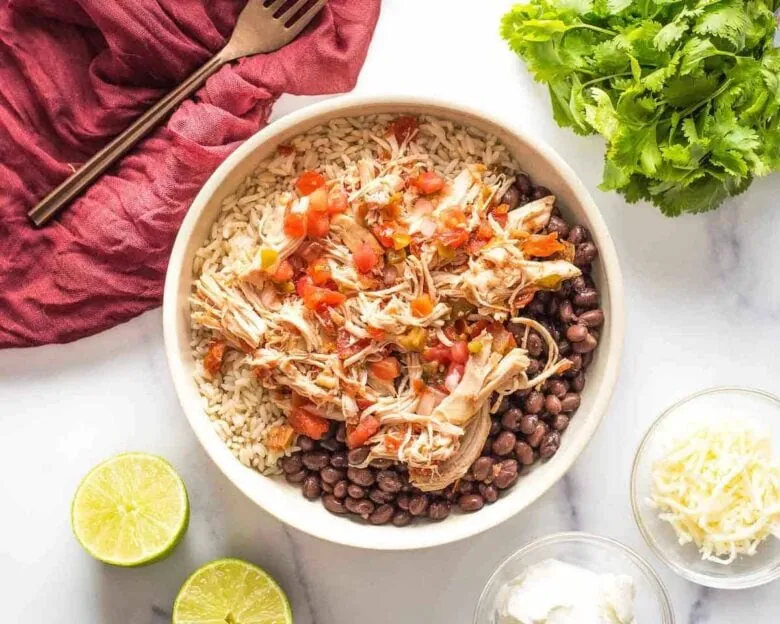 Mexican chicken rice in a white bowl with black beans and limes.