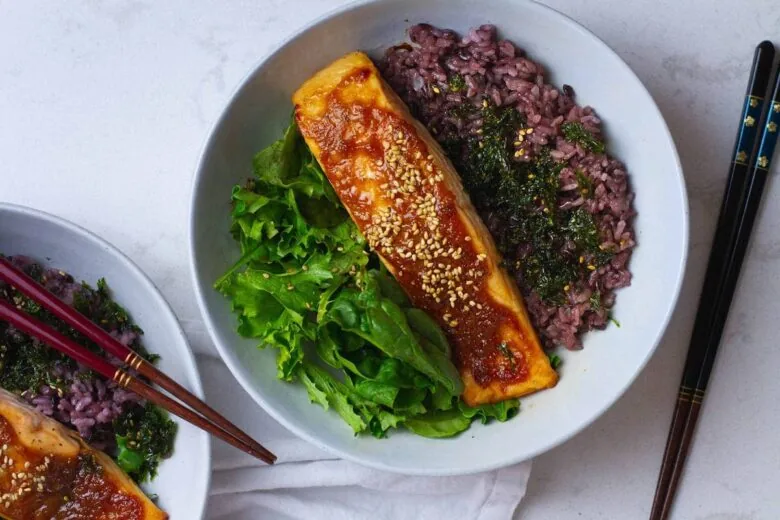 Two bowls of rice and salmon with greens and chopsticks.