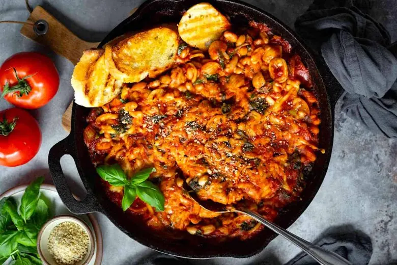 A skillet filled with pasta, tomatoes and bread.