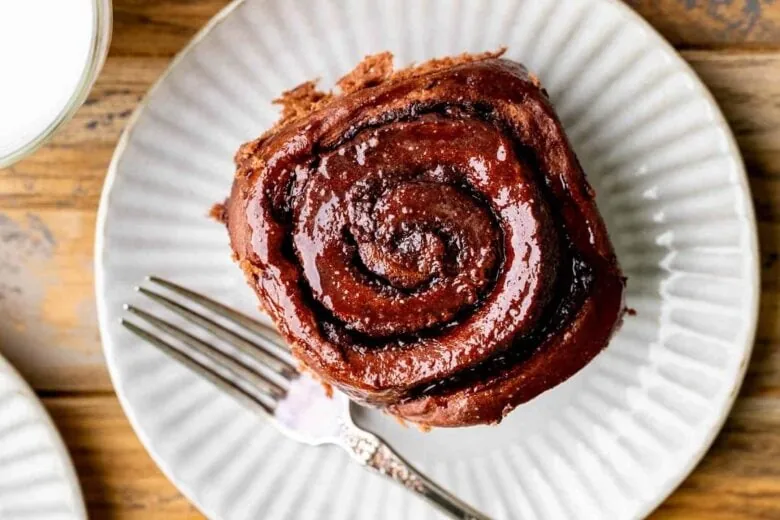 A chocolate cinnamon roll on a plate with a fork.