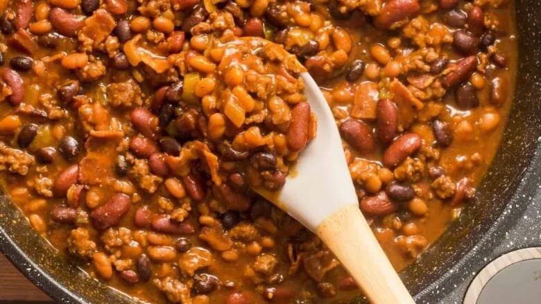 Chili beans in a skillet with a wooden spoon.