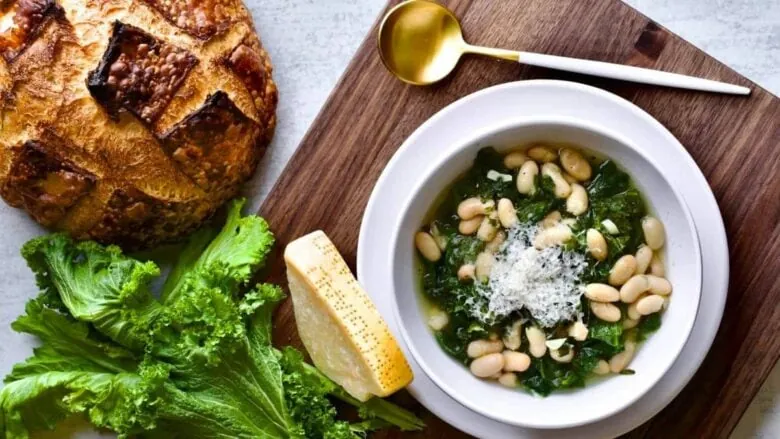 A bowl of white bean soup and bread on a cutting board.