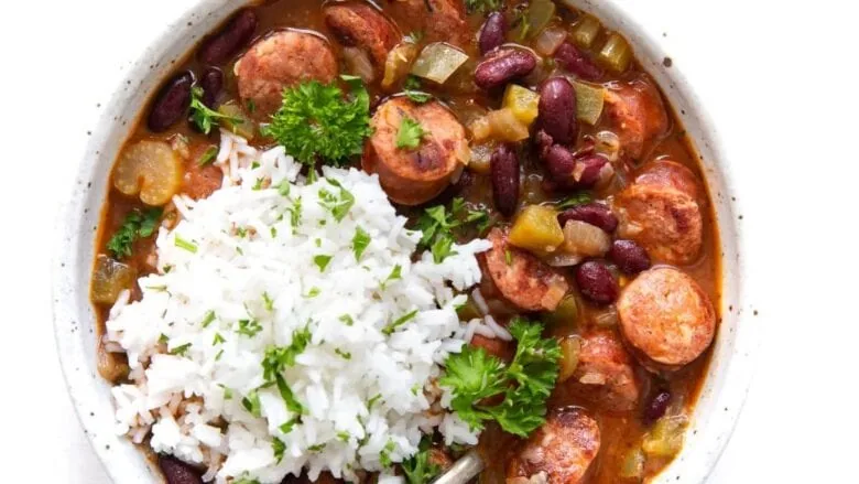 A bowl of rice, beans and sausage in a white bowl.