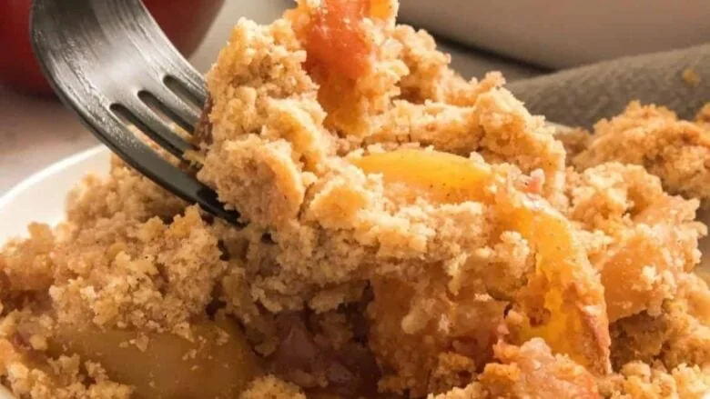 Peach crumble with a fork in a white bowl.