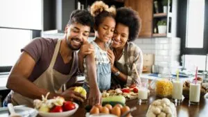 A family of three is preparing a meal together in a kitchen, incorporating an anti-inflammatory diet with various wholesome ingredients and two glasses of milk on the counter.