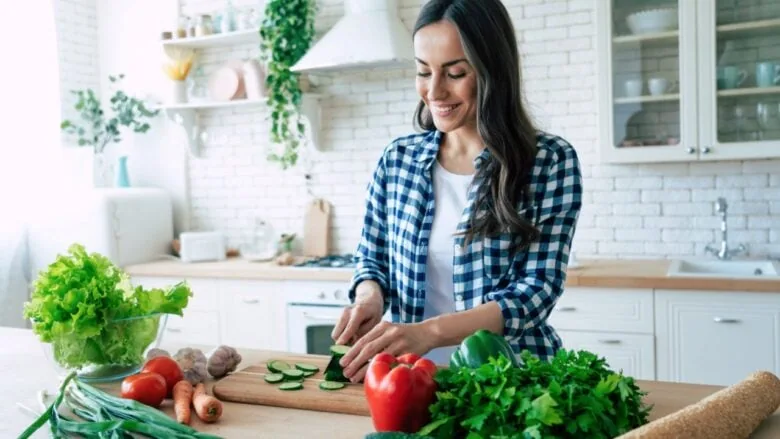 Woman cooking in a kitchen cutting cucumbers and vegetables.